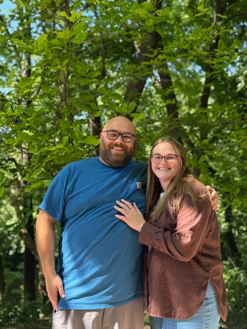 The happy couple smiling together in front of sunlit green trees